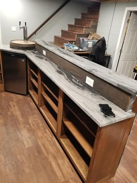 Wooden bar with concrete counter, shelves, and a tap system in a home basement setup.