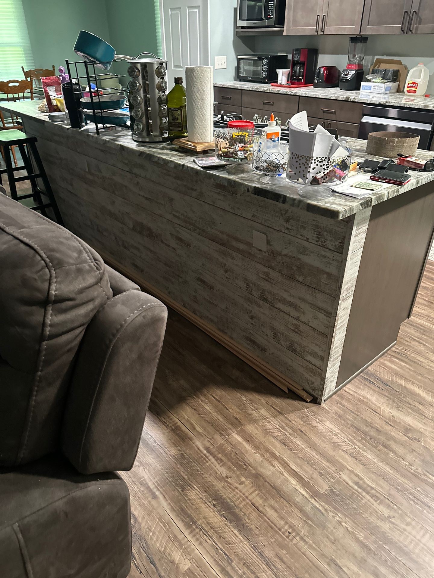 Kitchen with island cluttered with various household and kitchen items on wooden floor.