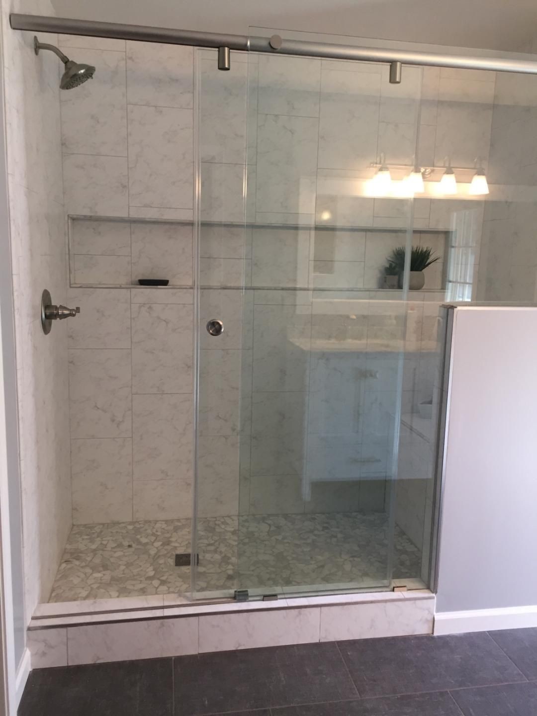 Modern bathroom with glass shower doors, white tiled walls, and pebble stone floor.